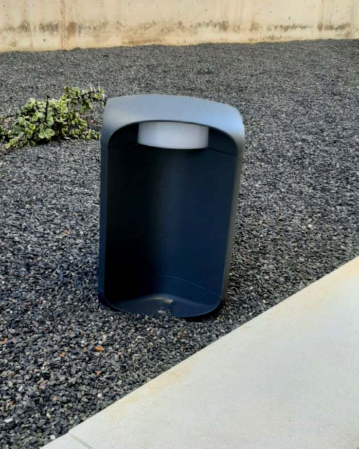 Baliza de jardín de aluminio gris instalada sobre grava, al lado de un muro de hormigón