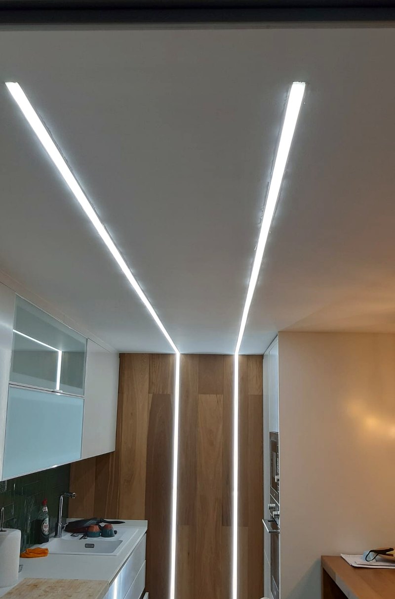Tiras de LED empotradas en línea en el techo de una cocina, que continúan bajando por el frente de un armario de madera