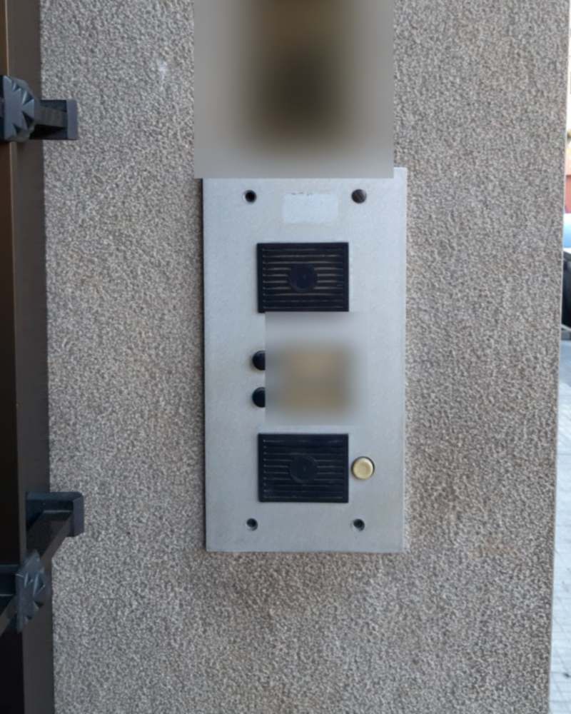 Placa de portero automático antigua en la entrada de un portal, de aluminio picado y con los rótulos amarillentos