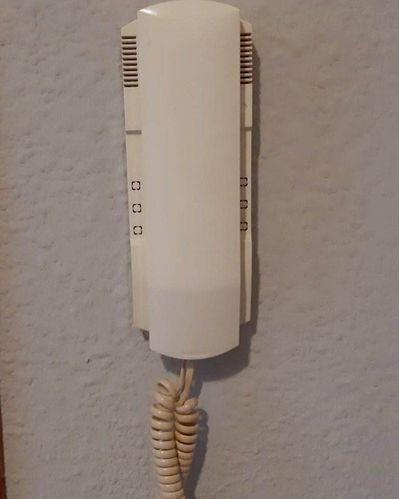 Telefonillo de portero automático antiguo, de plástico amarilleado, con el cable rizado colgando de la pared
